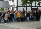 Menschen stehen im Freiluftbereich des Deutsch-Deutschen Museums Mödlareuth, einer Gedenkstätte zur deutschen Teilung, für ein Gruppenbild vor einem weißen Haus mit schwarzem Sichtfachwerk.