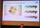 Frau Dr. Julia Kinigadner präsentiert eine Powerpoint-Folie mit der Überschrift "Nachhaltige urbane Mobiltätsplanung".